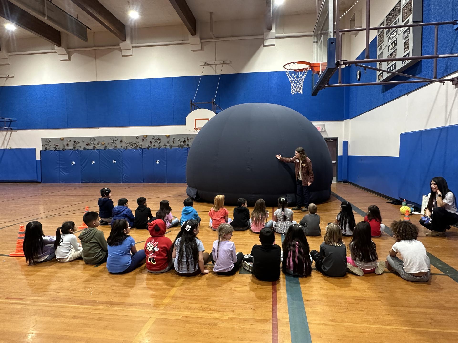 Kids in a gym at Wenatchee School District being instructed about WRI's Traveling Planetarium. 