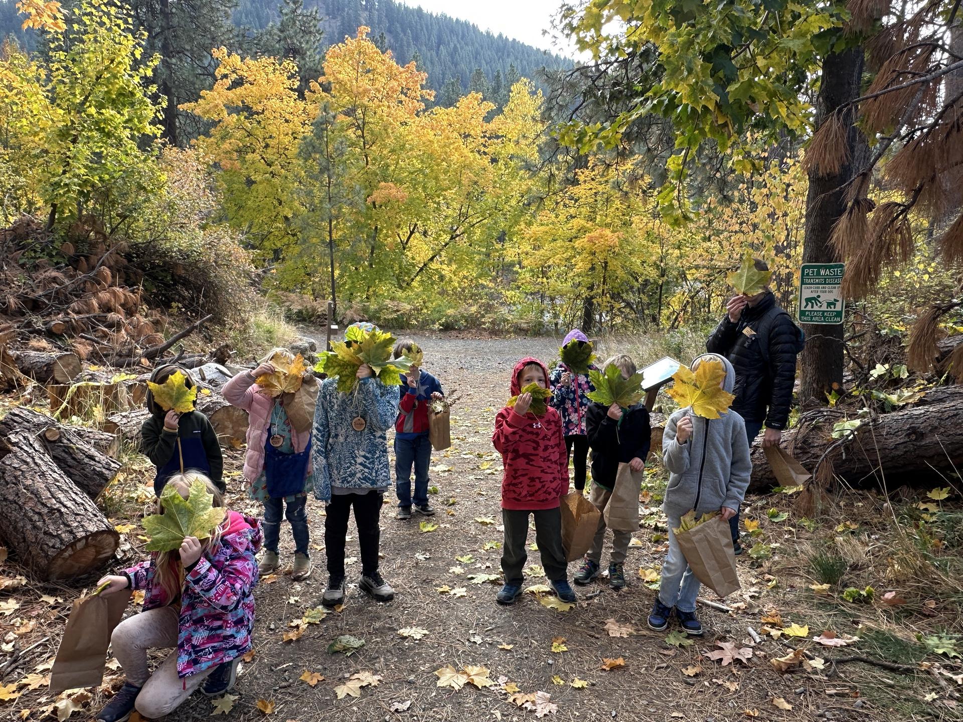 Fall Camp kids holding up leaves in front of their faces on the trails at WRI.