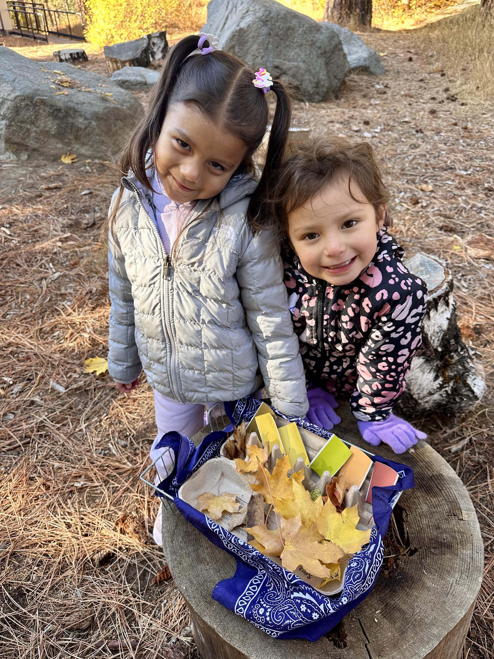 An image of 2 pre-k students exploring fall leaves.