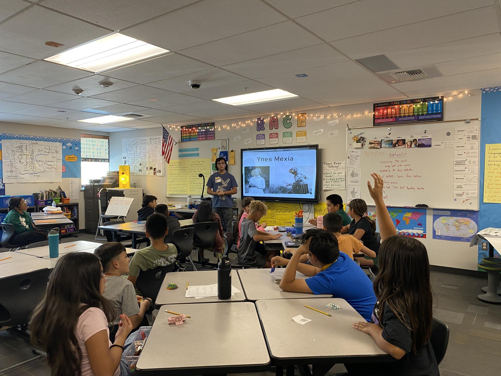 Traveling Naturalist in the Classroom with an educator standing at a projector screen teaching to students at desks.