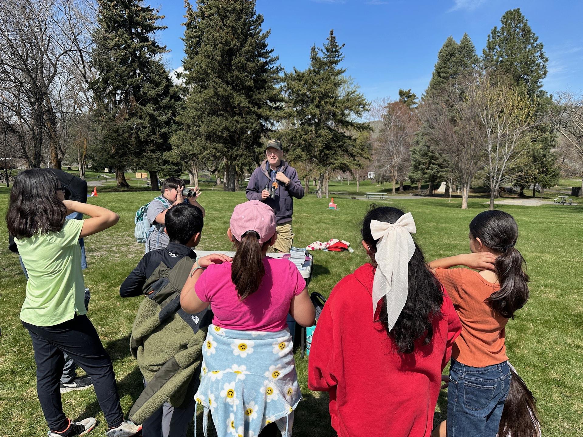 Image of students learning from an educator in a grassy field as part of the WRI Traveling Naturalist Program.