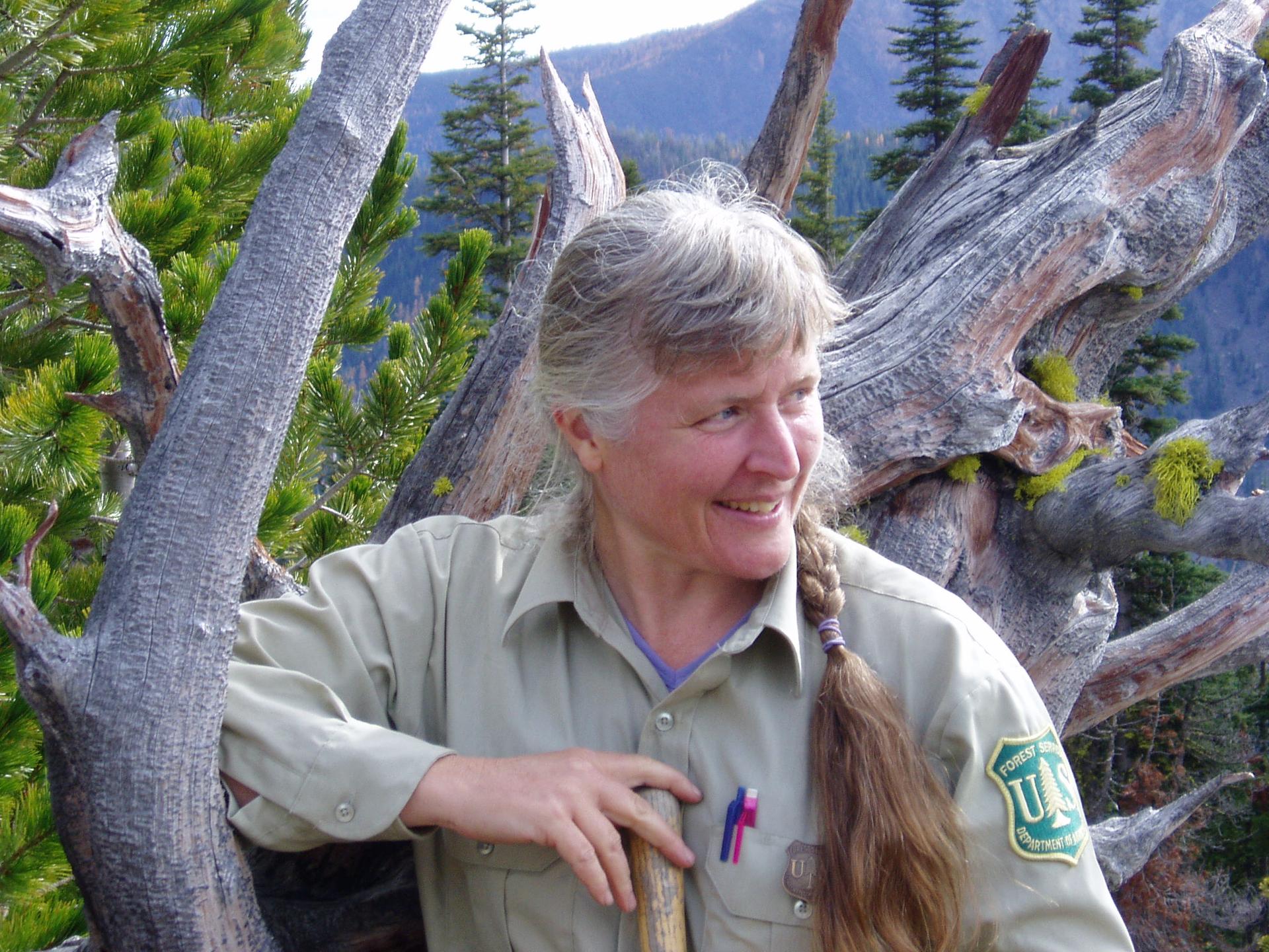 Picture of LIsa Therrell in her Forest Service uniform standing against a tree.