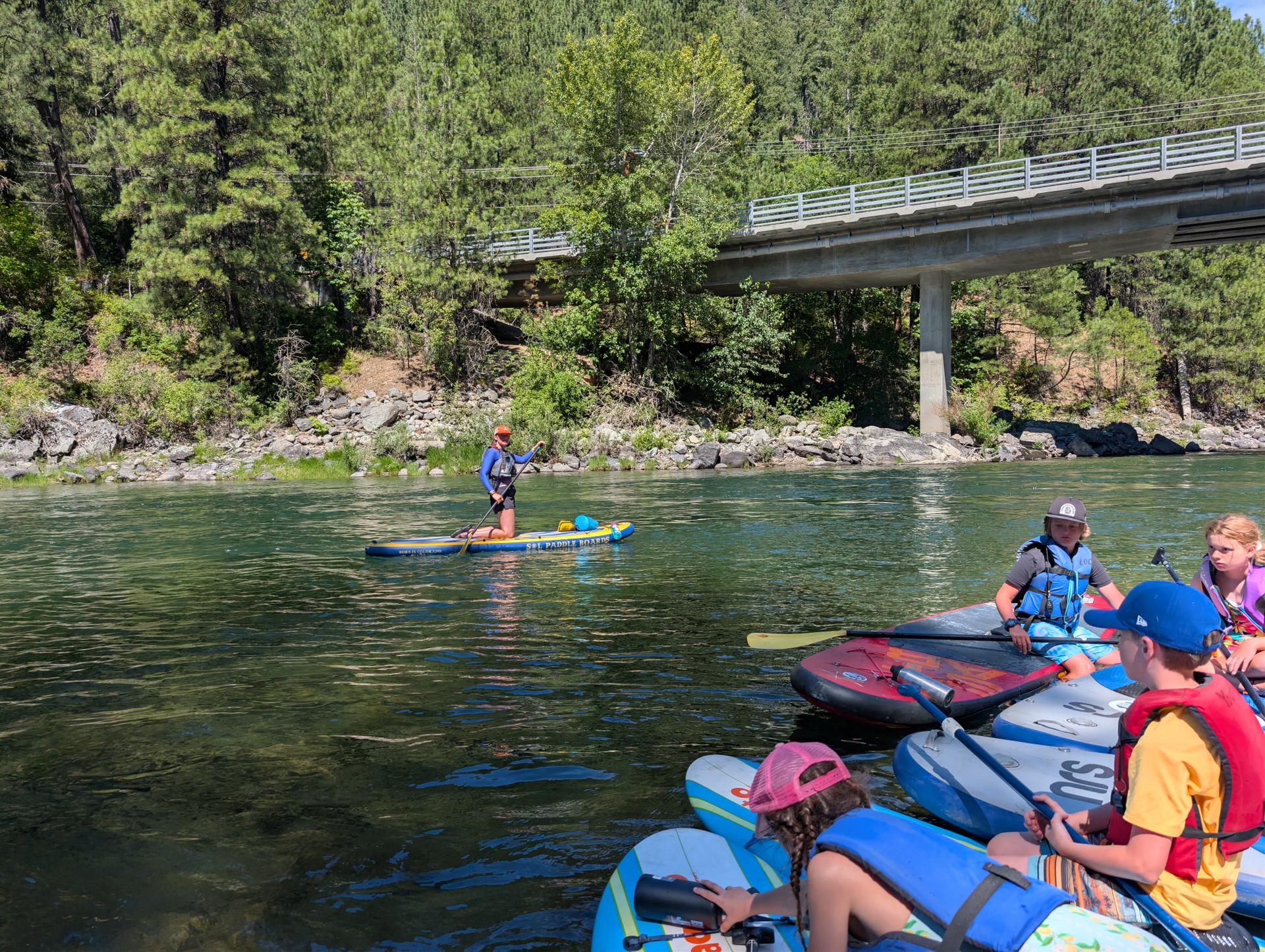River Wild 1 Camp on paddle board on the river. Educator is instructing the group of campers.