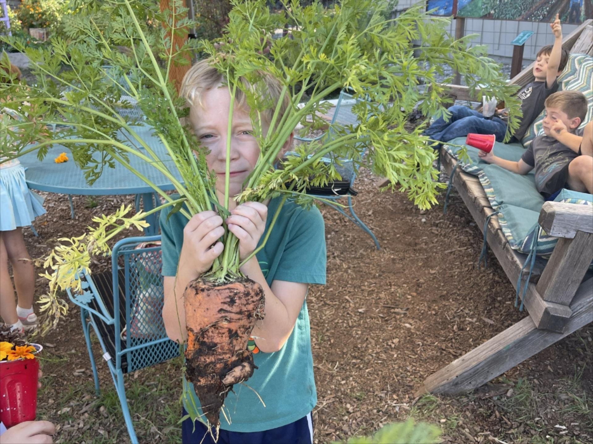 ASP student holding a large carrot grown in the Community Garden ASP plot.