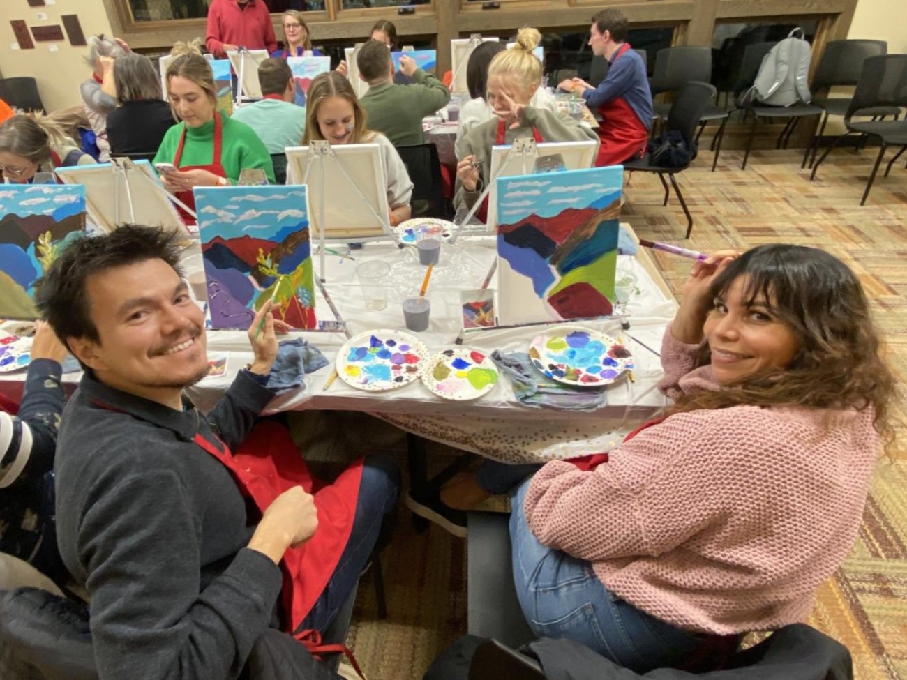 Two people posing with their paint brushes and their painted creations at a past Paint and Sip event. 