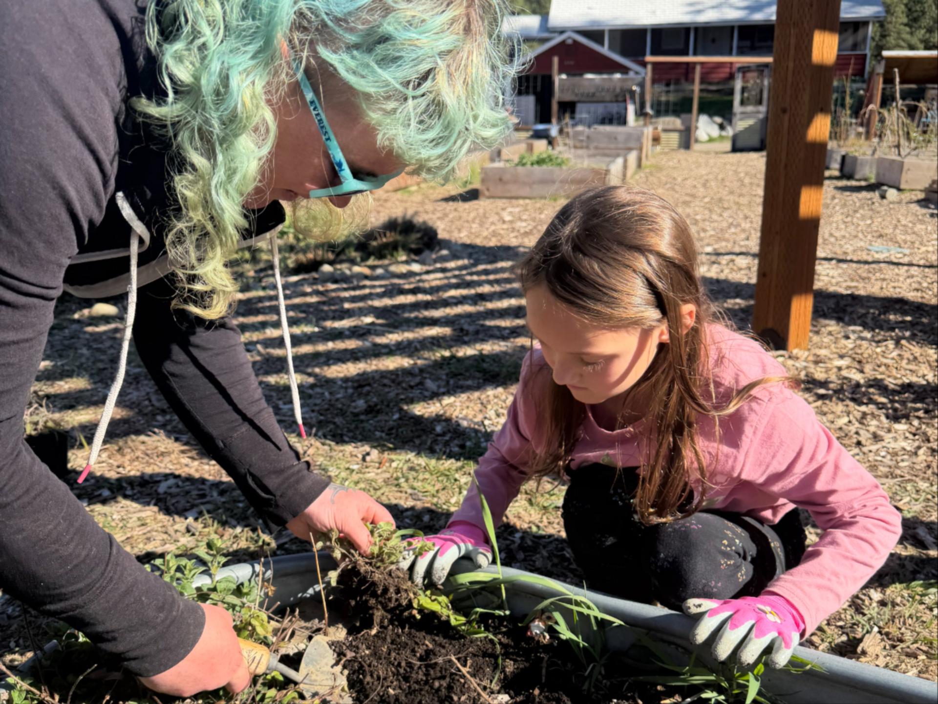 WRI After School Program student planting with Land Steward, Tiffa, in the Community Garden.